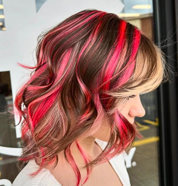 Side profile of a person with wavy, shoulder-length hair featuring dark brown, red, and pink highlights. Image links to Hair Cuttery's Instagram account.